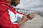 African-american man tapping fitness tracker after run by river bridge