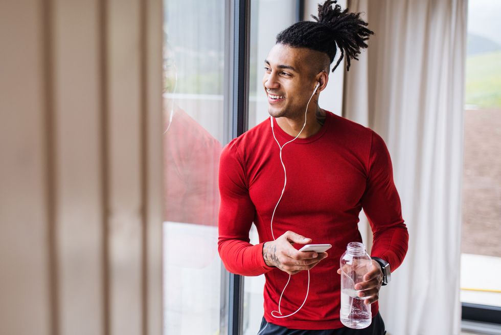 a portrait of fit mixed race man with smartphone and earphones at home, listening to music